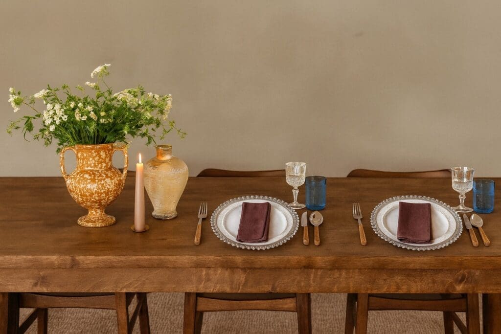 Dining table styled with stoneware plates, mauve napkins, and mixed glassware